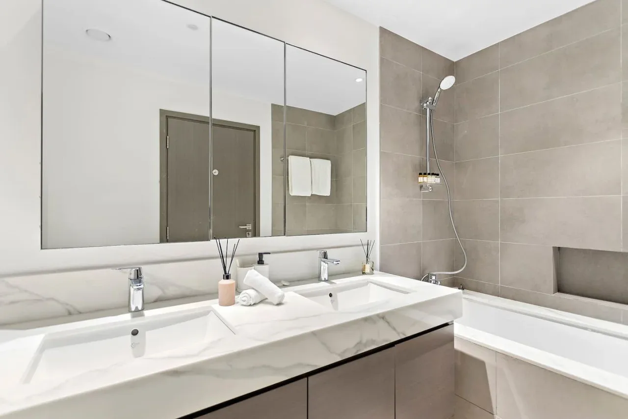 A bathroom vanity with a wide mirror sits beside a bathtub and shower.