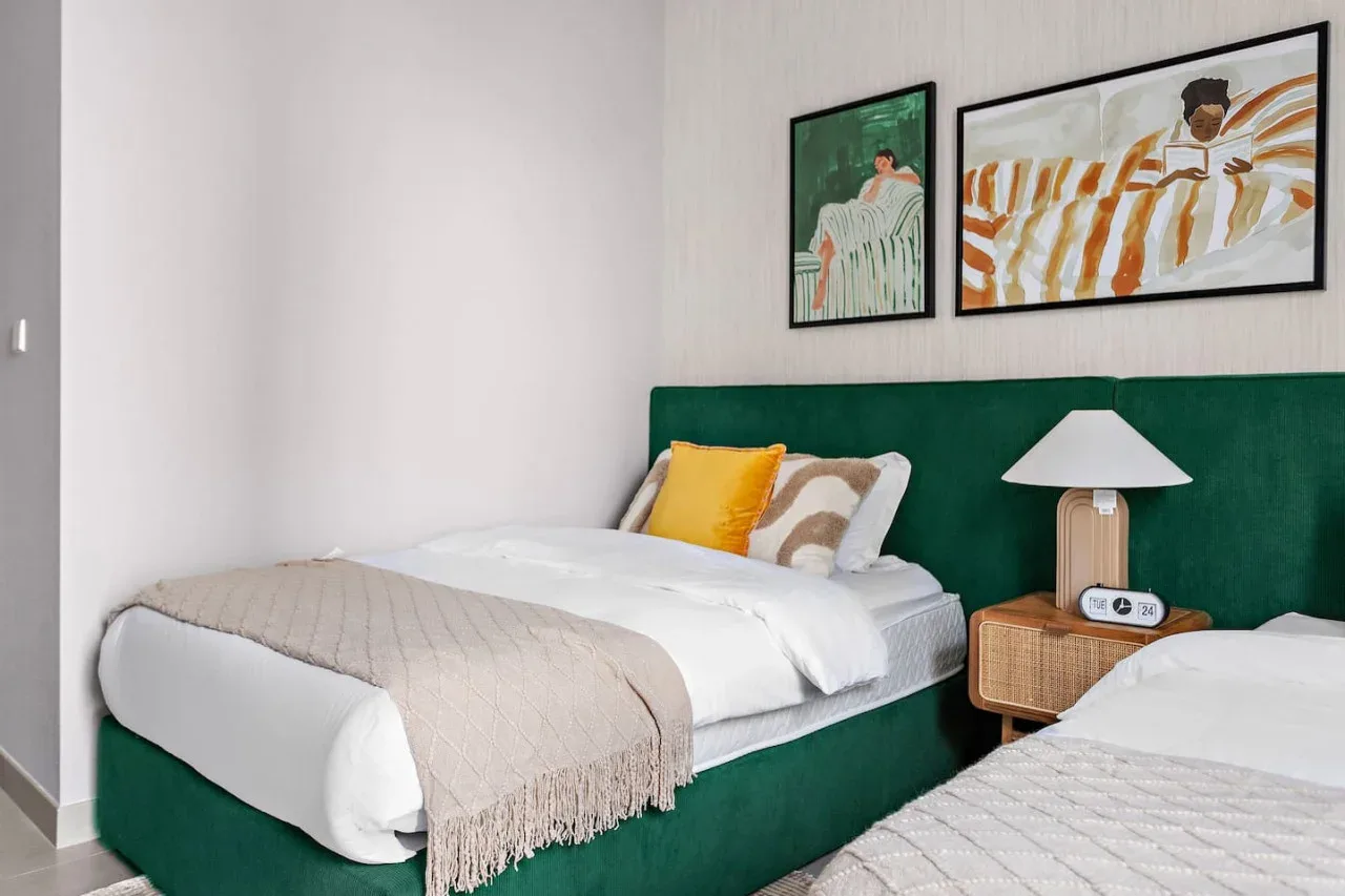 A bedroom with two beds, colorful pillows, and framed artwork above the headboard.