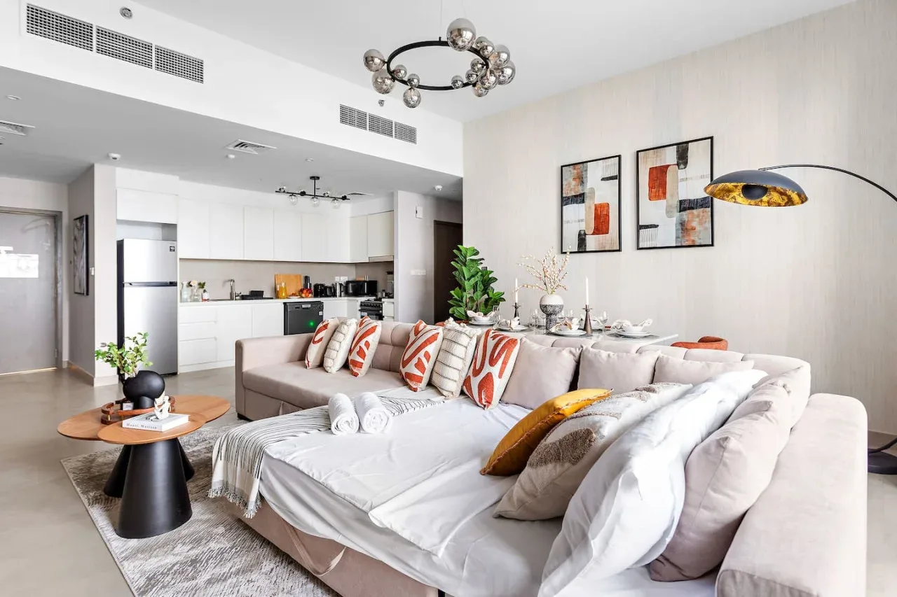 A bright open-plan living room with a large sectional and a kitchen behind it.