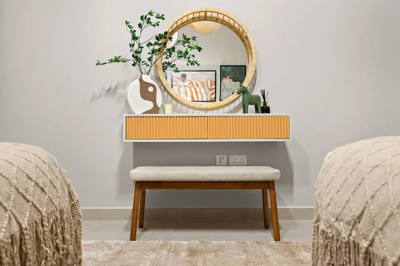 A bedroom vanity with a round mirror, floating shelf, and cushioned bench.