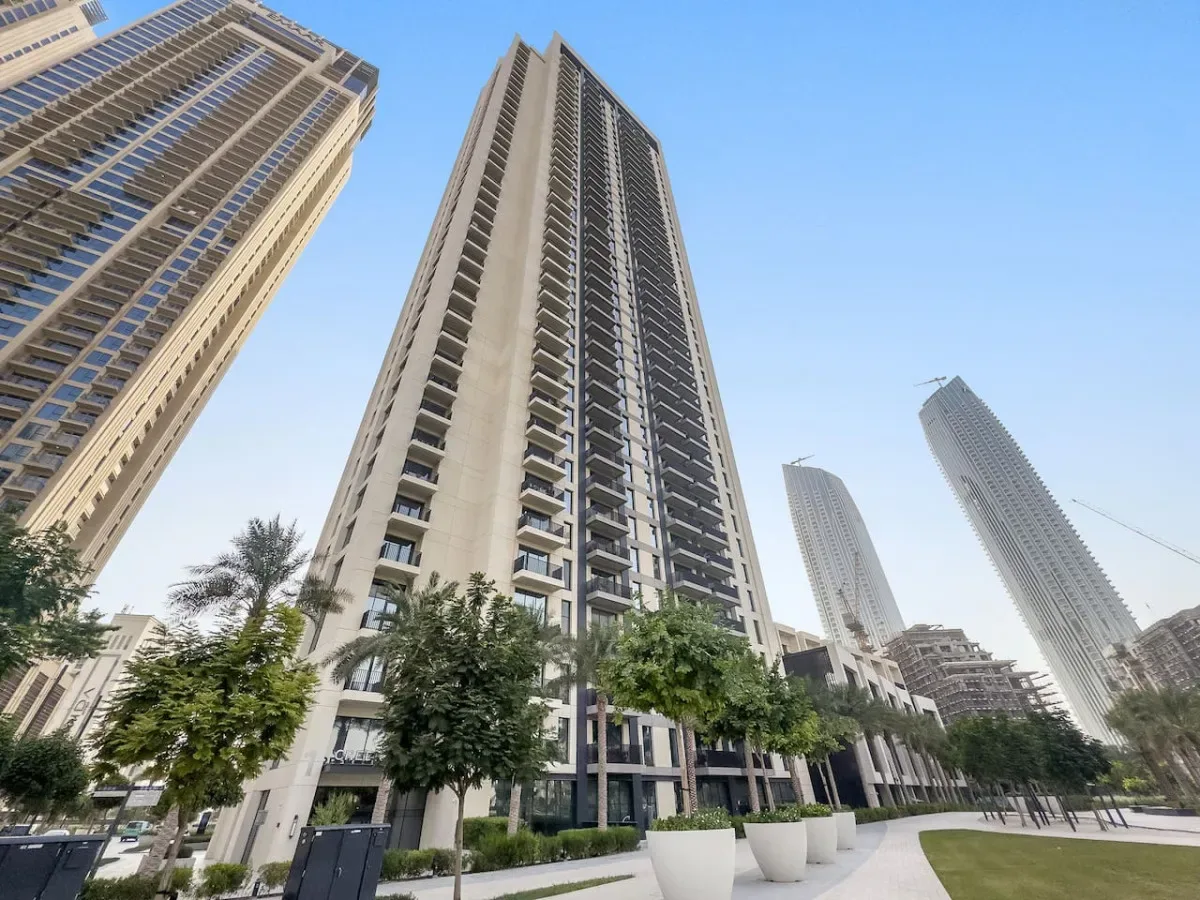 Tall residential towers rise above trees and a landscaped pedestrian walkway.