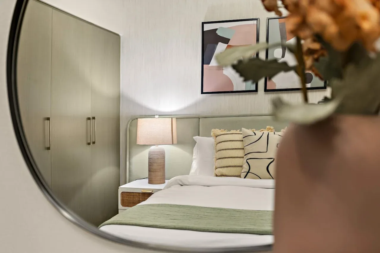A bedroom reflected in a mirror, with a bed and bedside lamp.