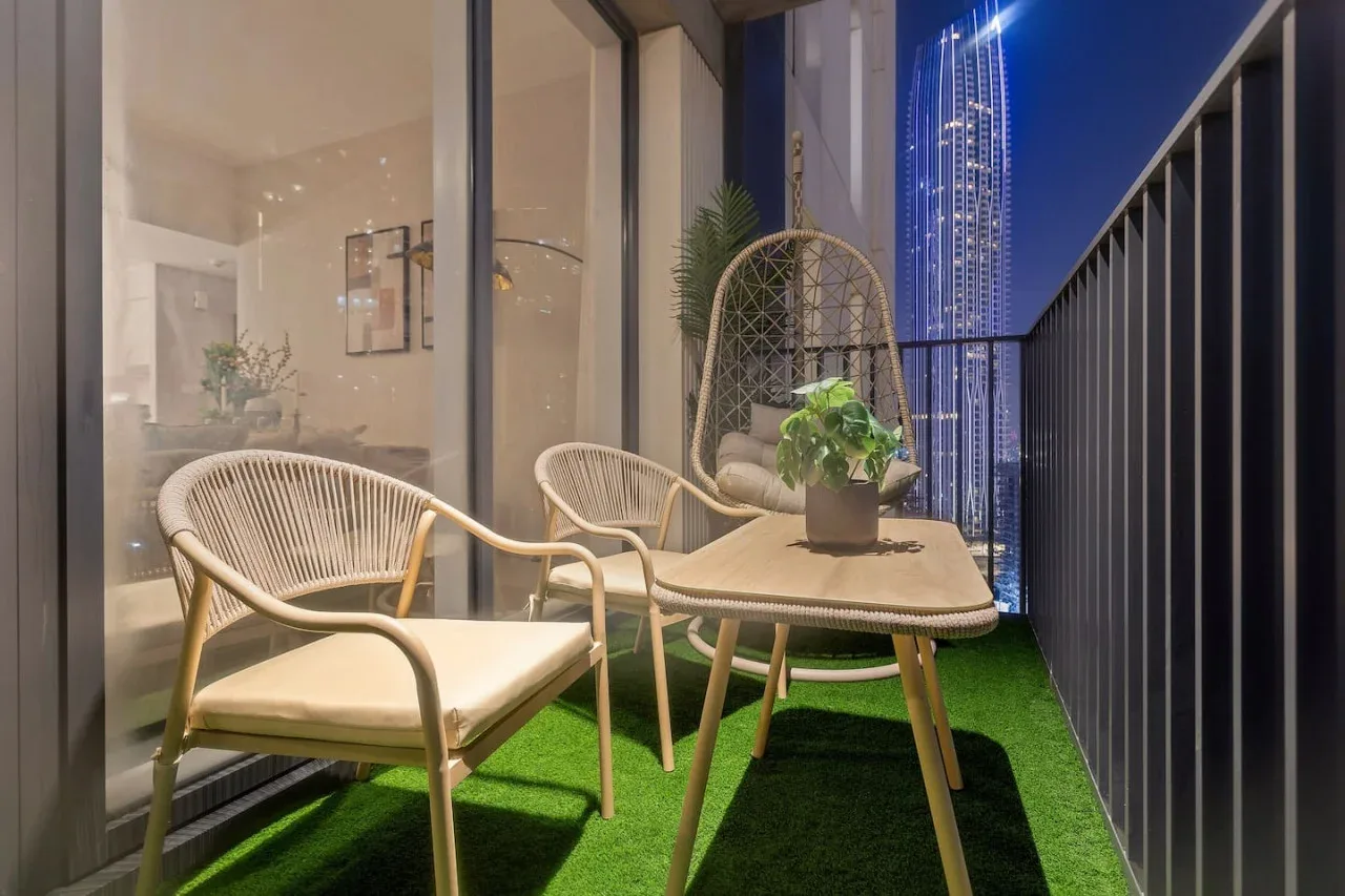 A balcony seating area with a small table, potted plant, and city view at night.
