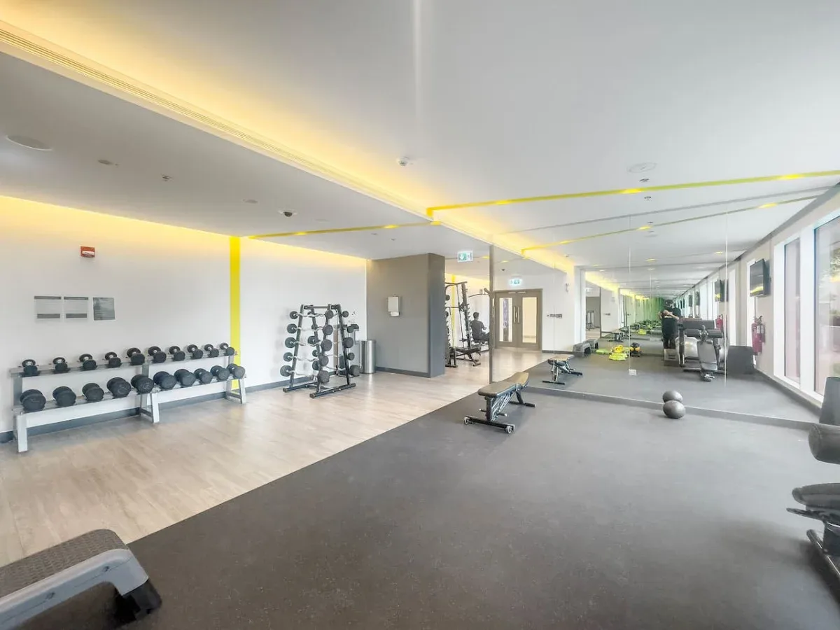 A bright gym with exercise machines and rows of weights.