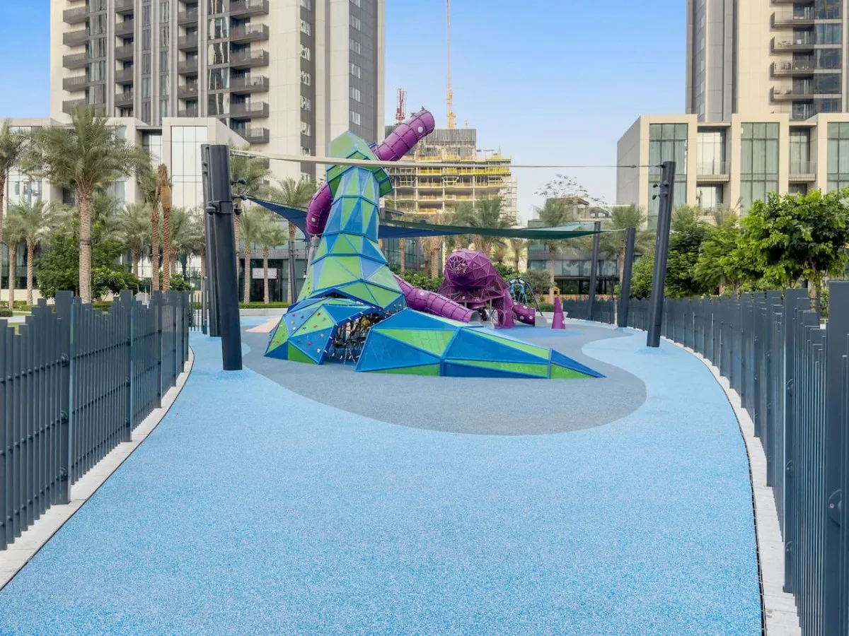 An outdoor playground features a colorful climbing structure on a blue play surface.
