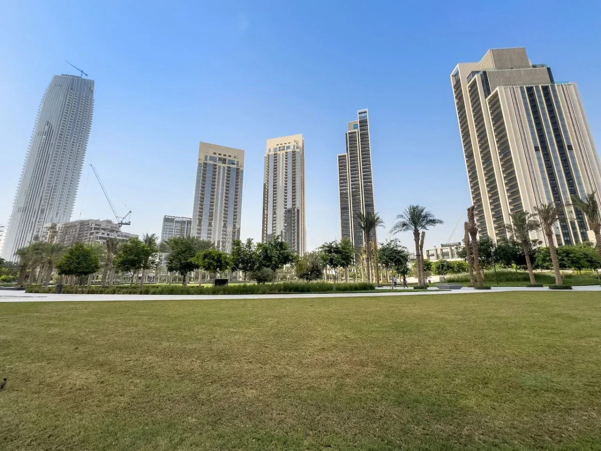 A city park lawn sits in front of modern high-rise buildings and palm trees.
