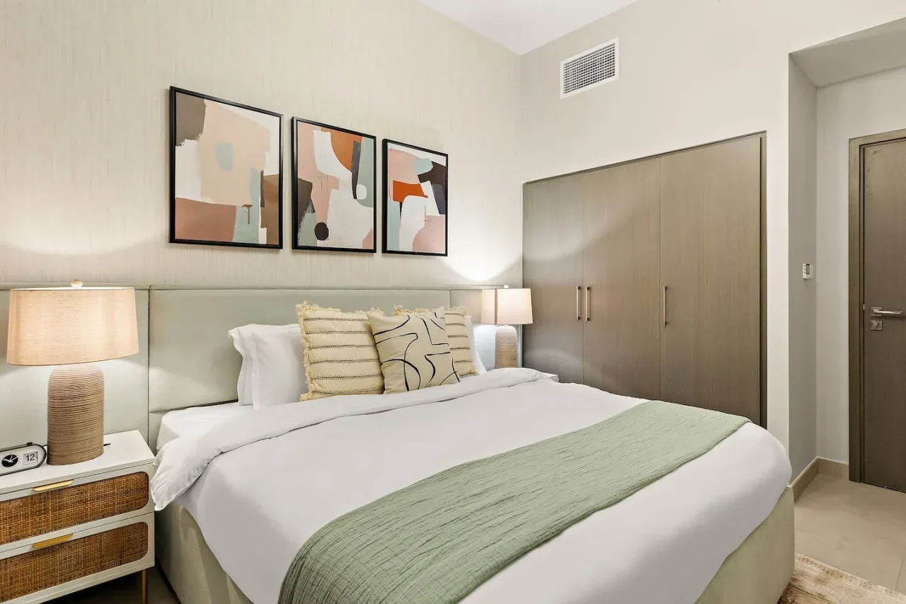 A bedroom with a neatly made bed, framed artwork, and bedside lamps.