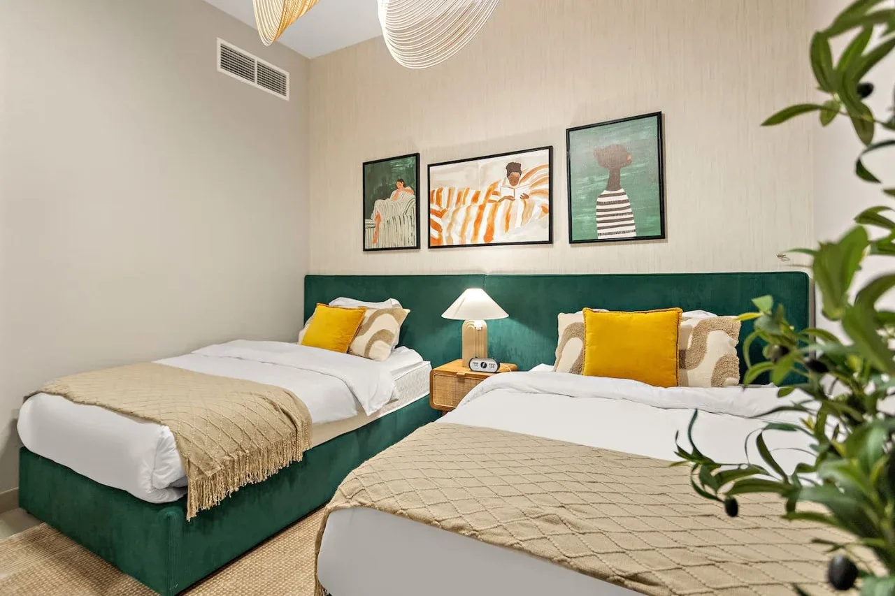 A bedroom with two beds, yellow pillows, and framed artwork above the headboard.