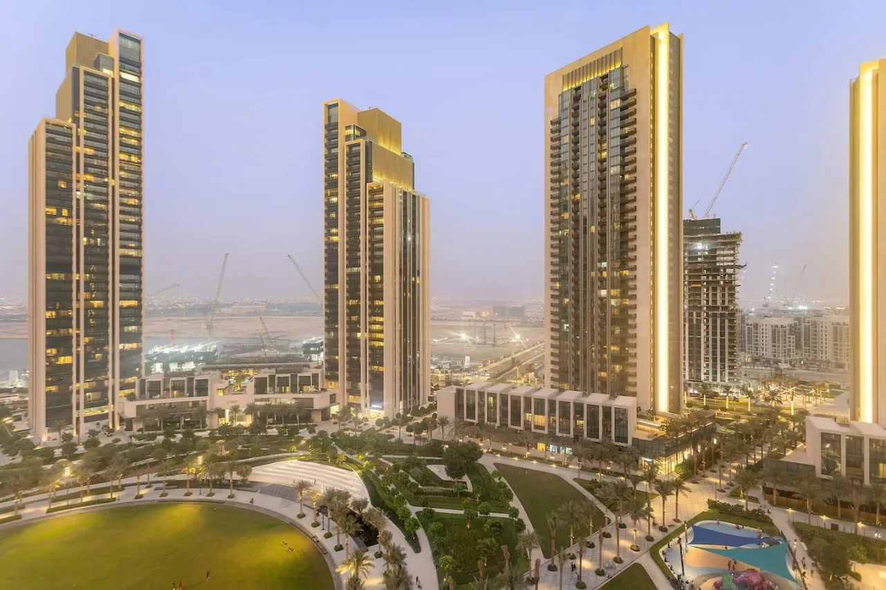 A modern city skyline with illuminated high-rise buildings and landscaped grounds.