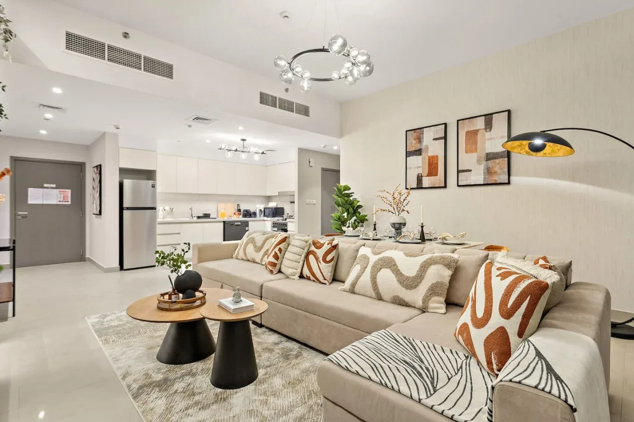 A bright open-plan living room with a sectional seating area and adjoining kitchen.