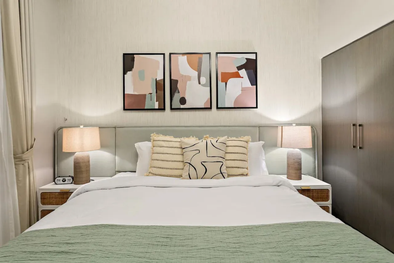 A bedroom with a neatly made bed and abstract artwork above the headboard.