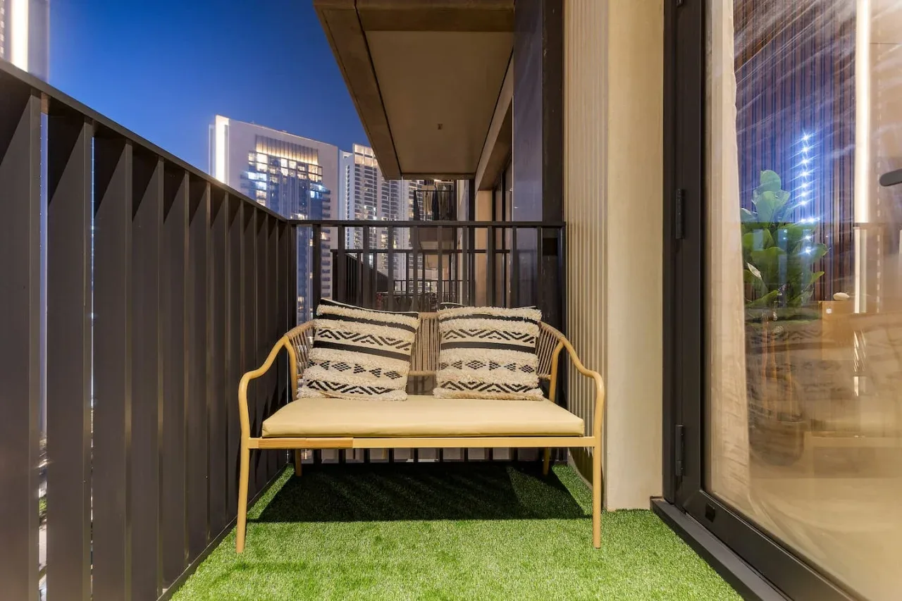 A small balcony with a cushioned bench and artificial grass flooring.