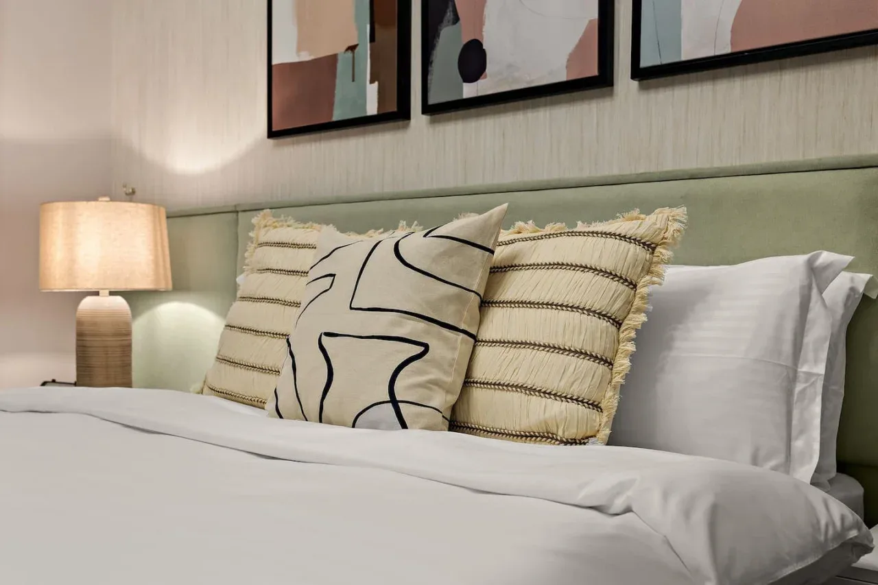 A bedroom with a neatly made bed, decorative pillows, and a bedside lamp.