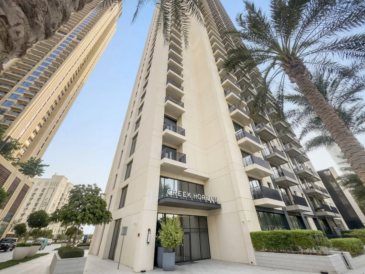 A tall apartment building entrance with balconies and palm trees.
