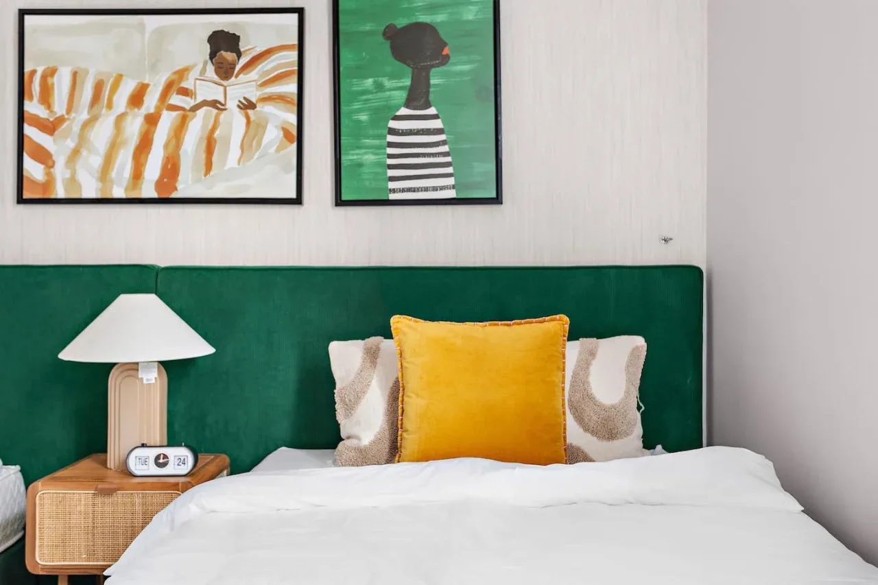 A bedroom with a neatly made bed, green headboard, and framed artwork.
