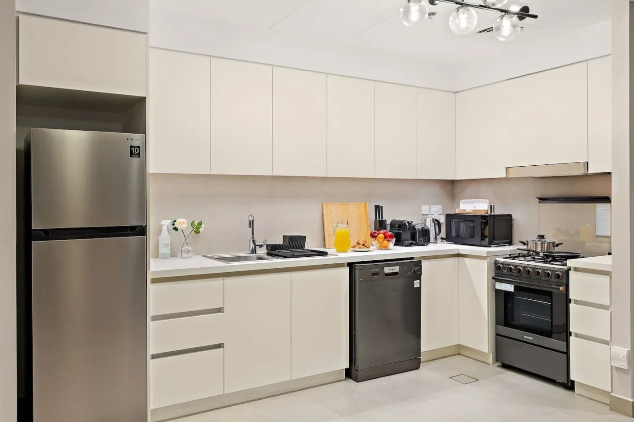 A modern kitchen with pale cabinets, a refrigerator, and countertop appliances.