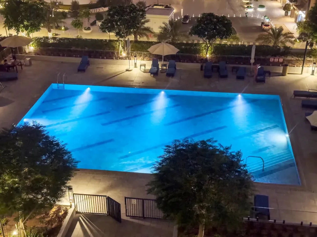 Una piscina exterior iluminada por la noche, rodeada de asientos reclinables.