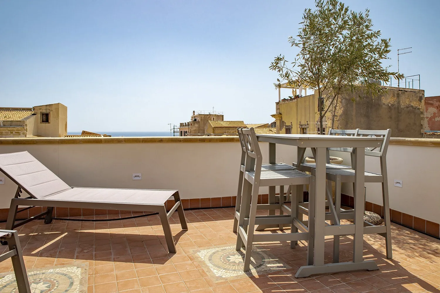 Una terraza embaldosada con asientos al aire libre y una mesa frente a edificios cercanos.