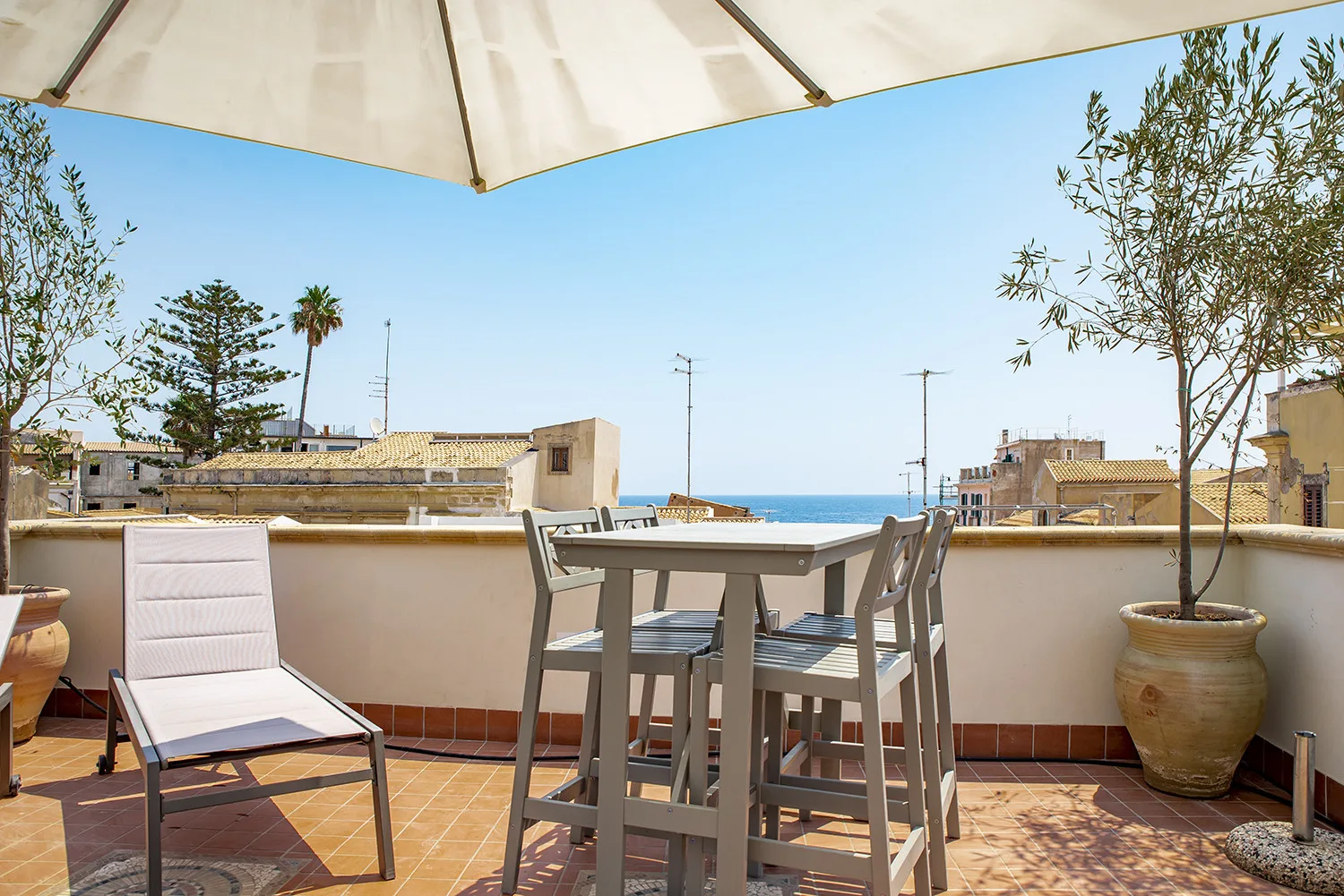 Una terraza en la azotea con mesa y sillas de comedor frente al mar.