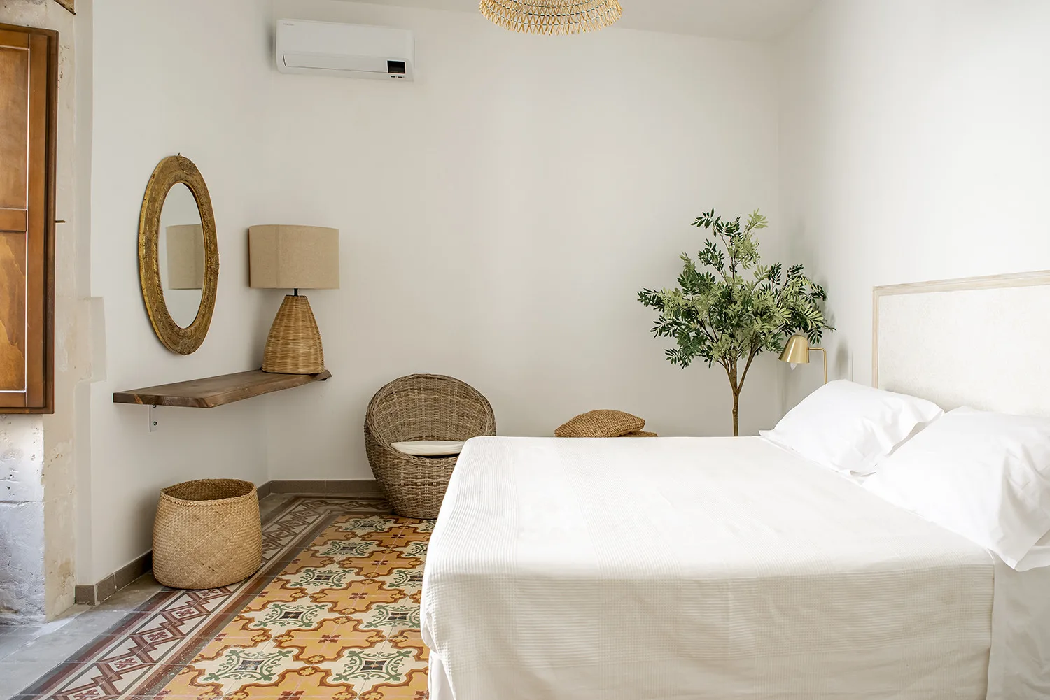 Un dormitorio con una cama blanca, suelo de baldosas estampadas y un árbol en maceta.