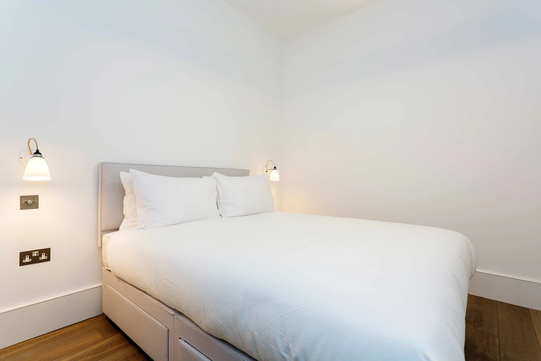 Un dormitorio con una cama vestida de blanco y luces en la pared.