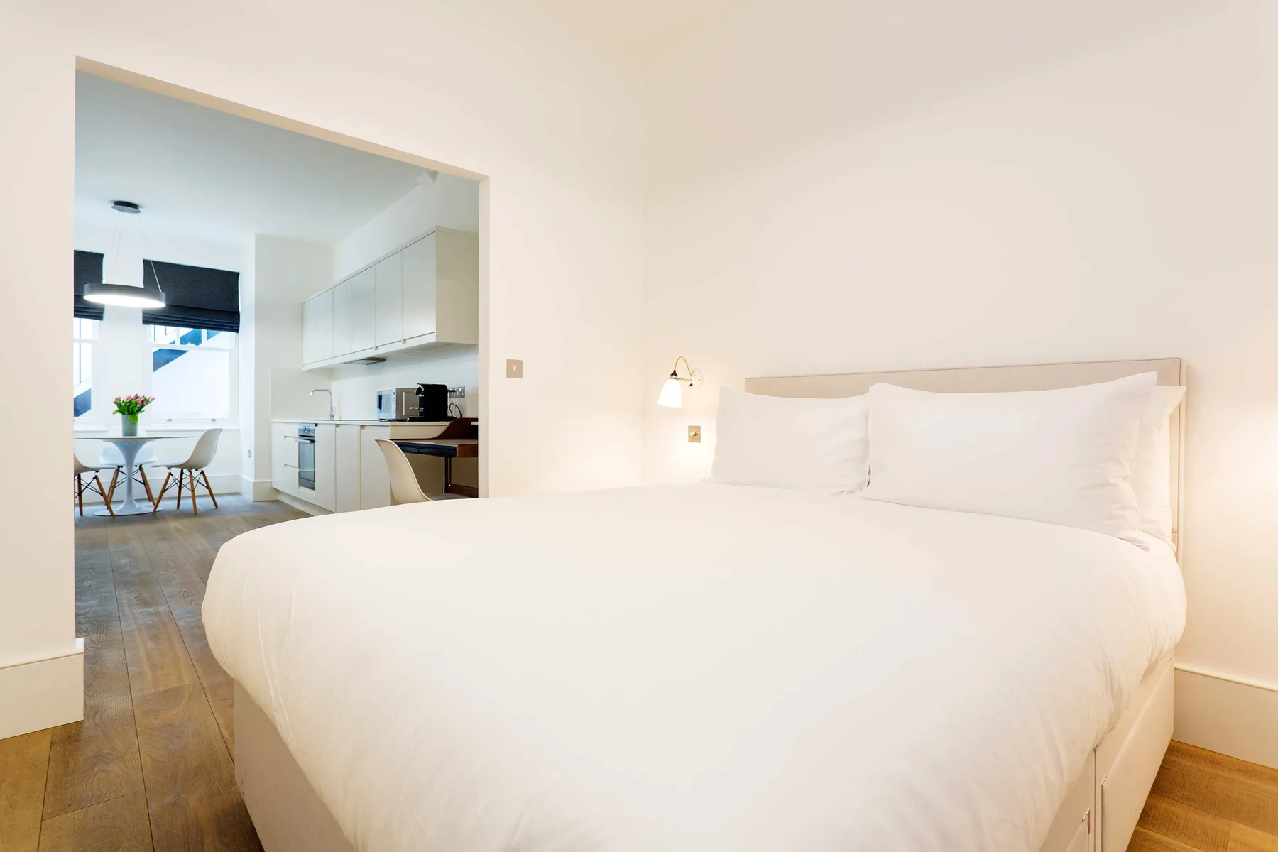 Dormitorio luminoso con una cama grande y vista abierta a una cocina y comedor.