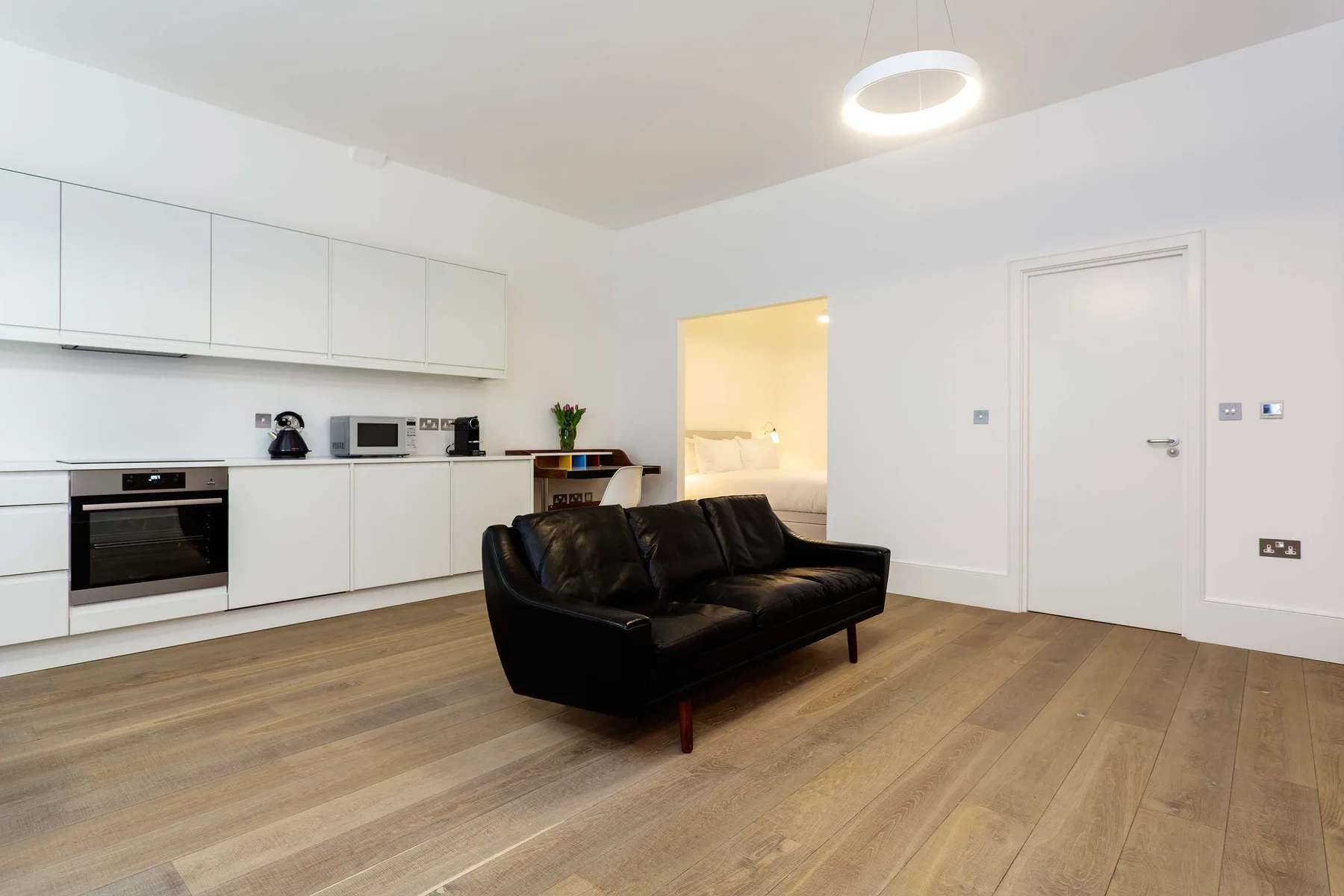 A modern living area with black seating beside a white kitchen.