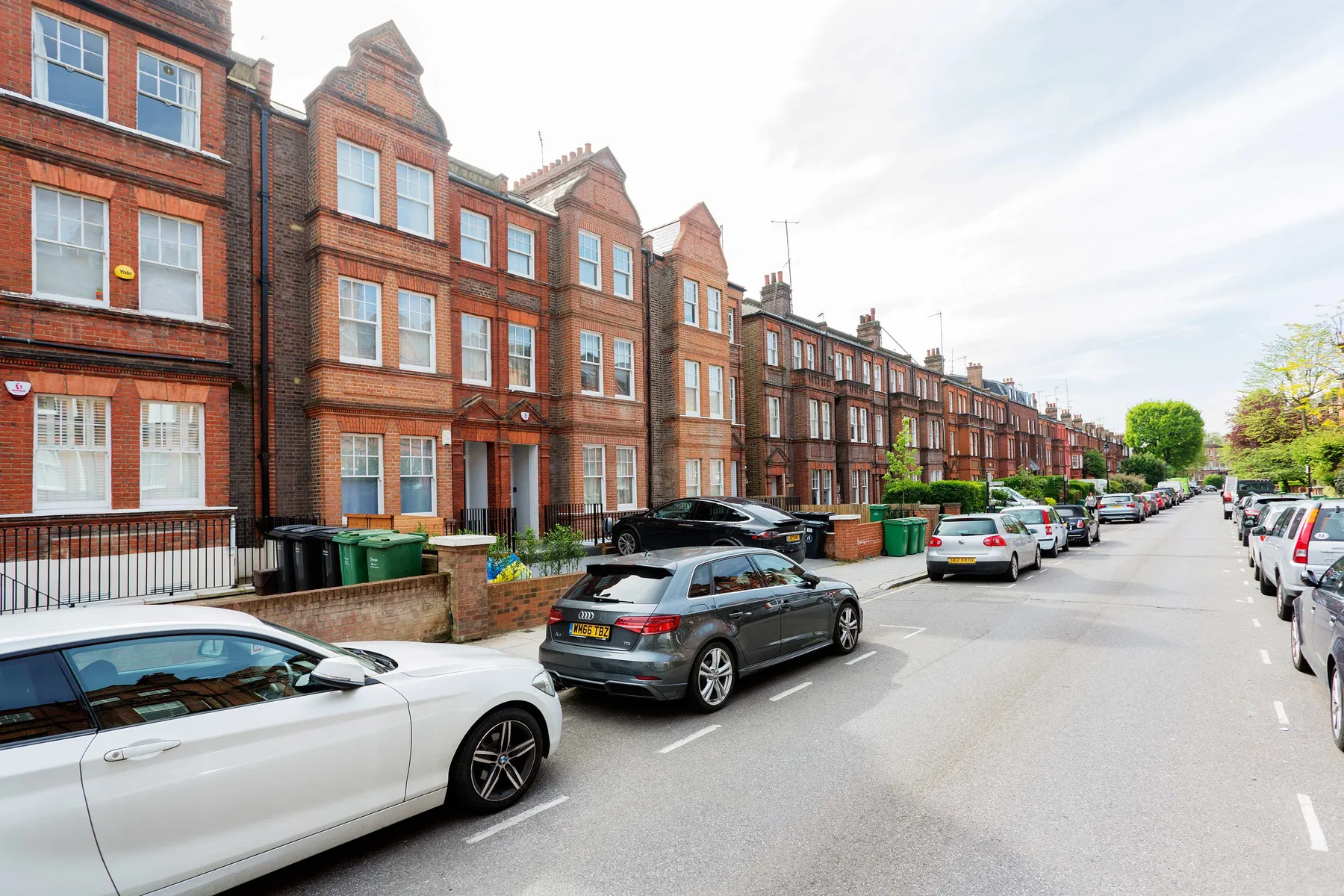 A residential street lined with red-brick townhouses and parked cars.