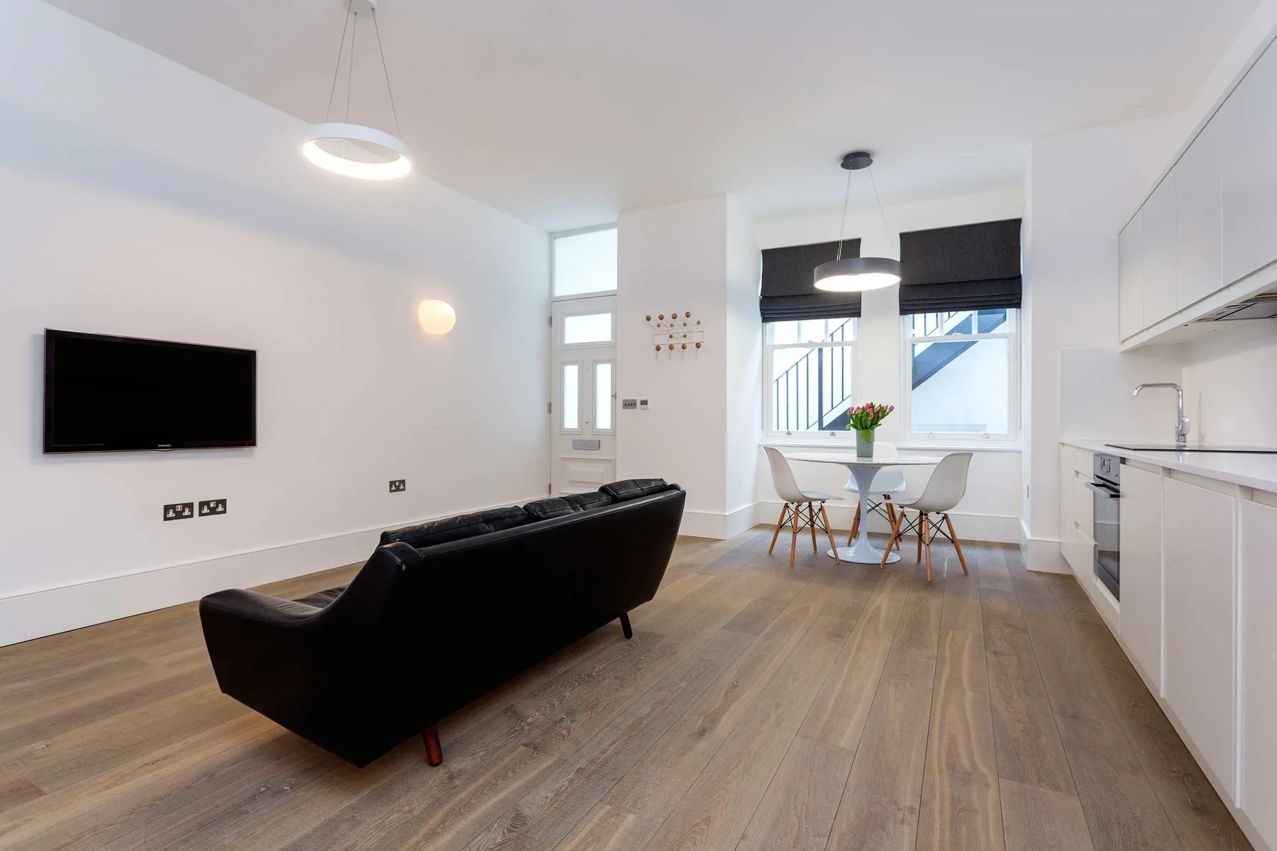 Bright living area with a black sofa, dining table, and kitchen.