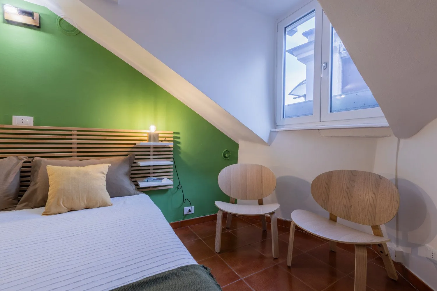 A bedroom with a bed and two chairs beneath a sloped ceiling.