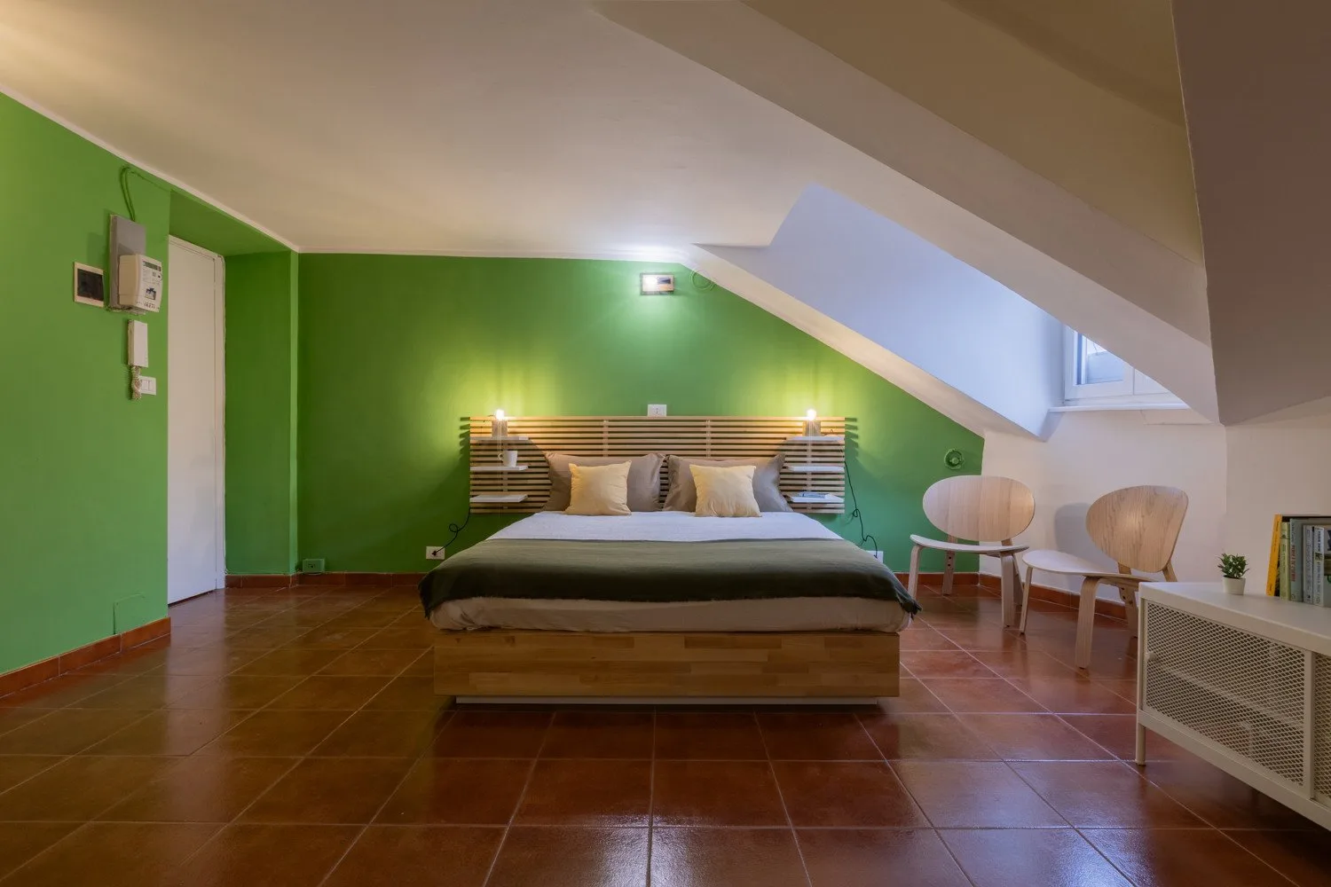 A bedroom with a bed beneath a sloped ceiling and green walls.