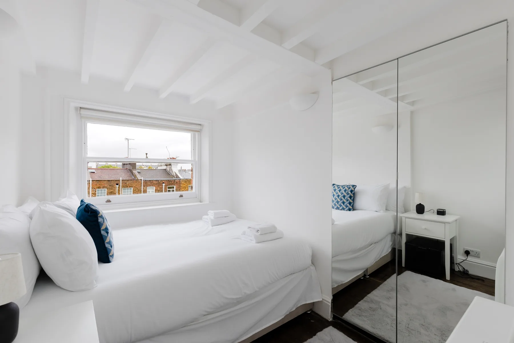 Dormitorio luminoso con una cama blanca y puertas de armario con espejo.