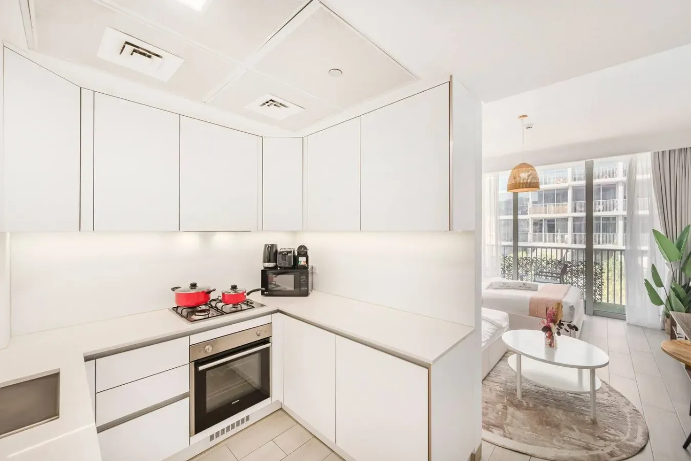 A modern white kitchen opens onto a bright living area with a round table.