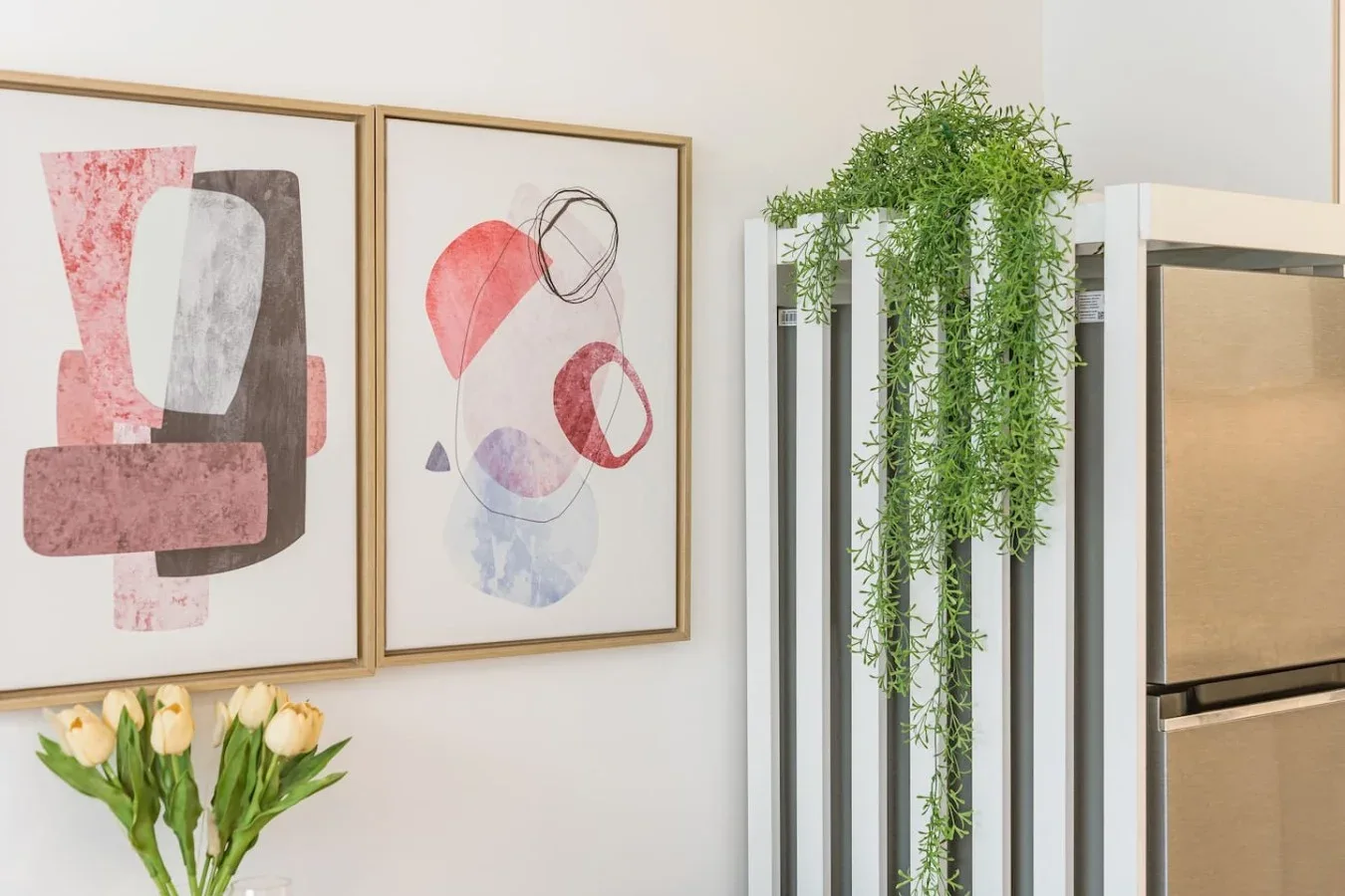 A bright interior corner features abstract framed artwork and a trailing green plant.