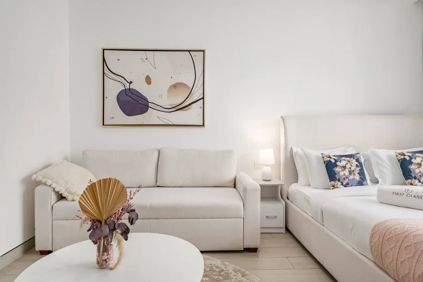 A bright bedroom with a bed, seating, and framed abstract artwork.