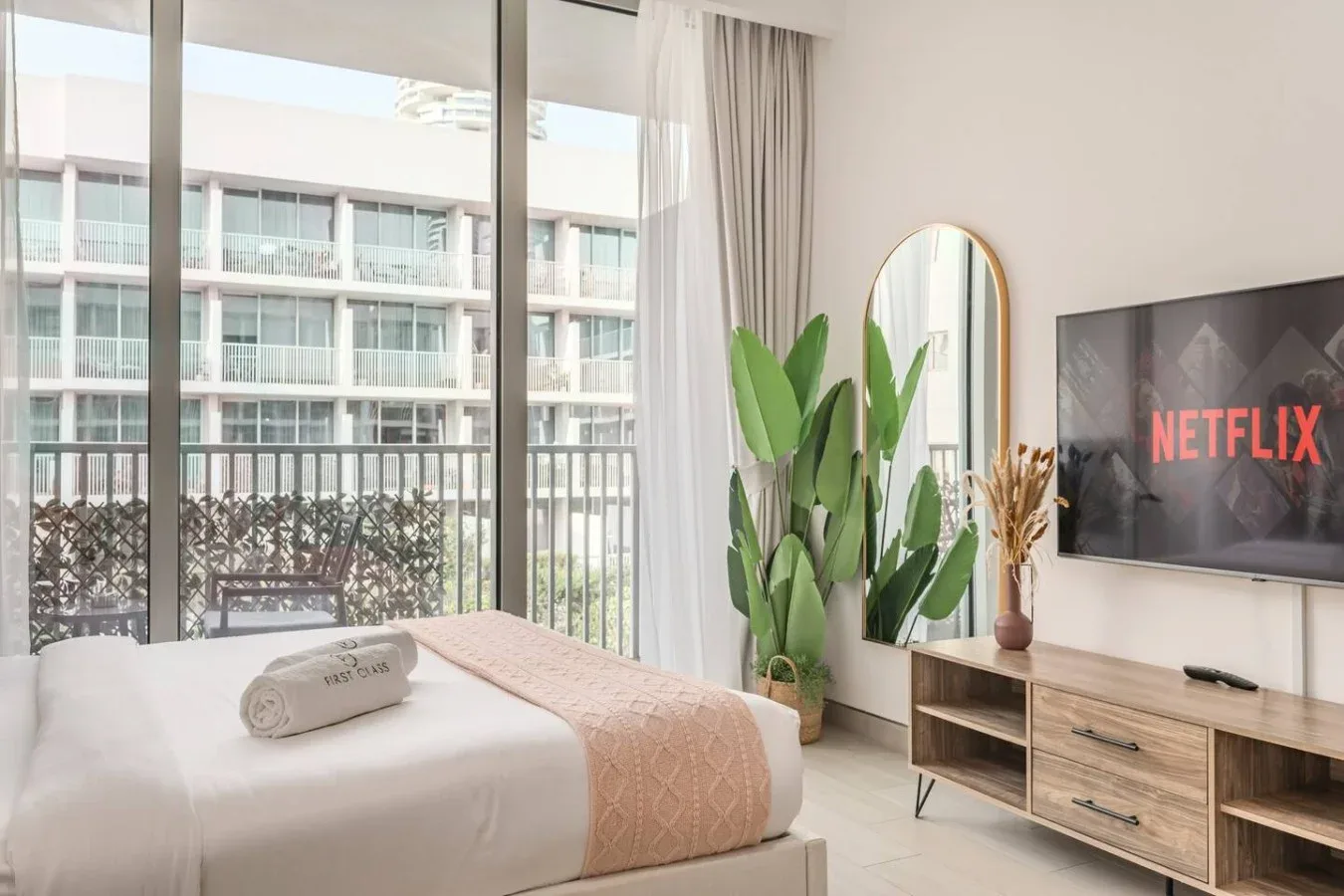 A bright studio bedroom with a bed, large windows, and a television.