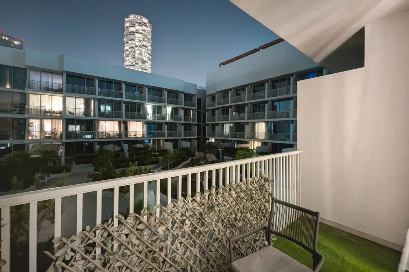 A balcony overlooks a landscaped courtyard and surrounding apartment buildings at dusk.