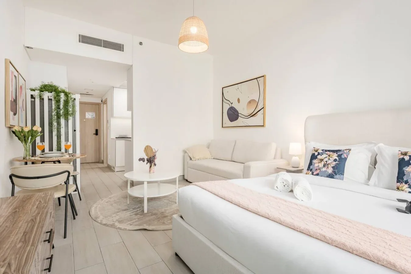 A bright studio bedroom with a bed, seating area, and dining table.