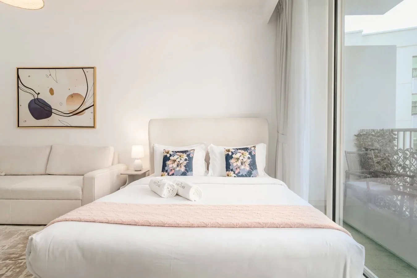 A bright bedroom with a neatly made bed and a sofa beside it.