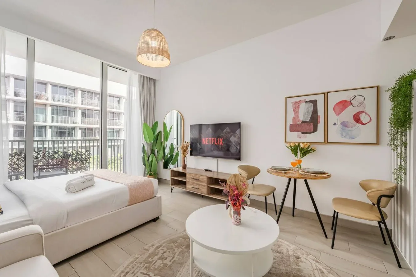 A bright studio room with a bed, seating area, and large windows.