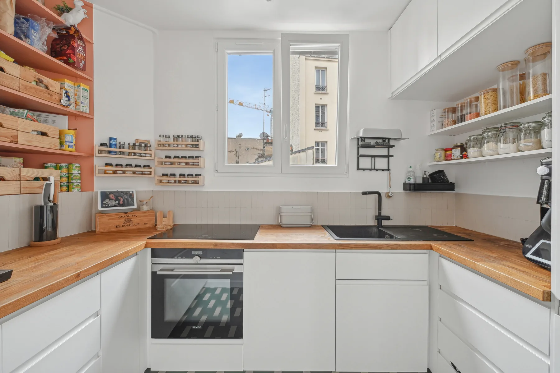 A bright kitchen with wooden countertops, white cabinets, and a central window.