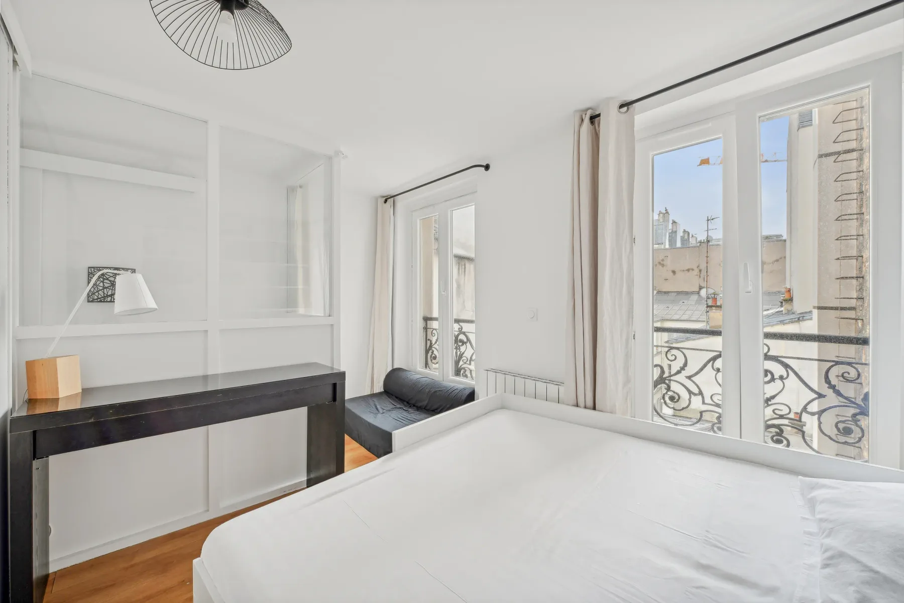 A bright bedroom with a bed, desk, and doors opening onto a balcony.