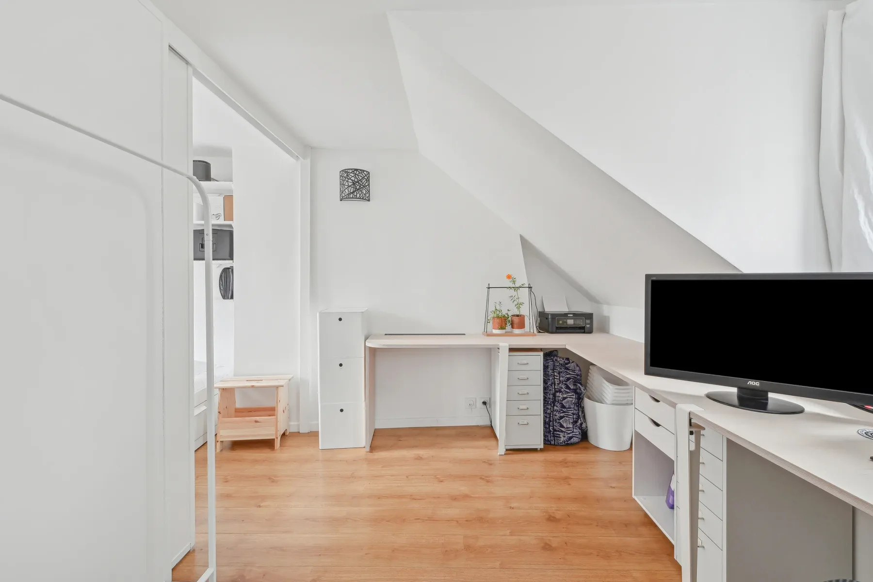 A compact attic workspace with a desk, storage cabinets, and a television.