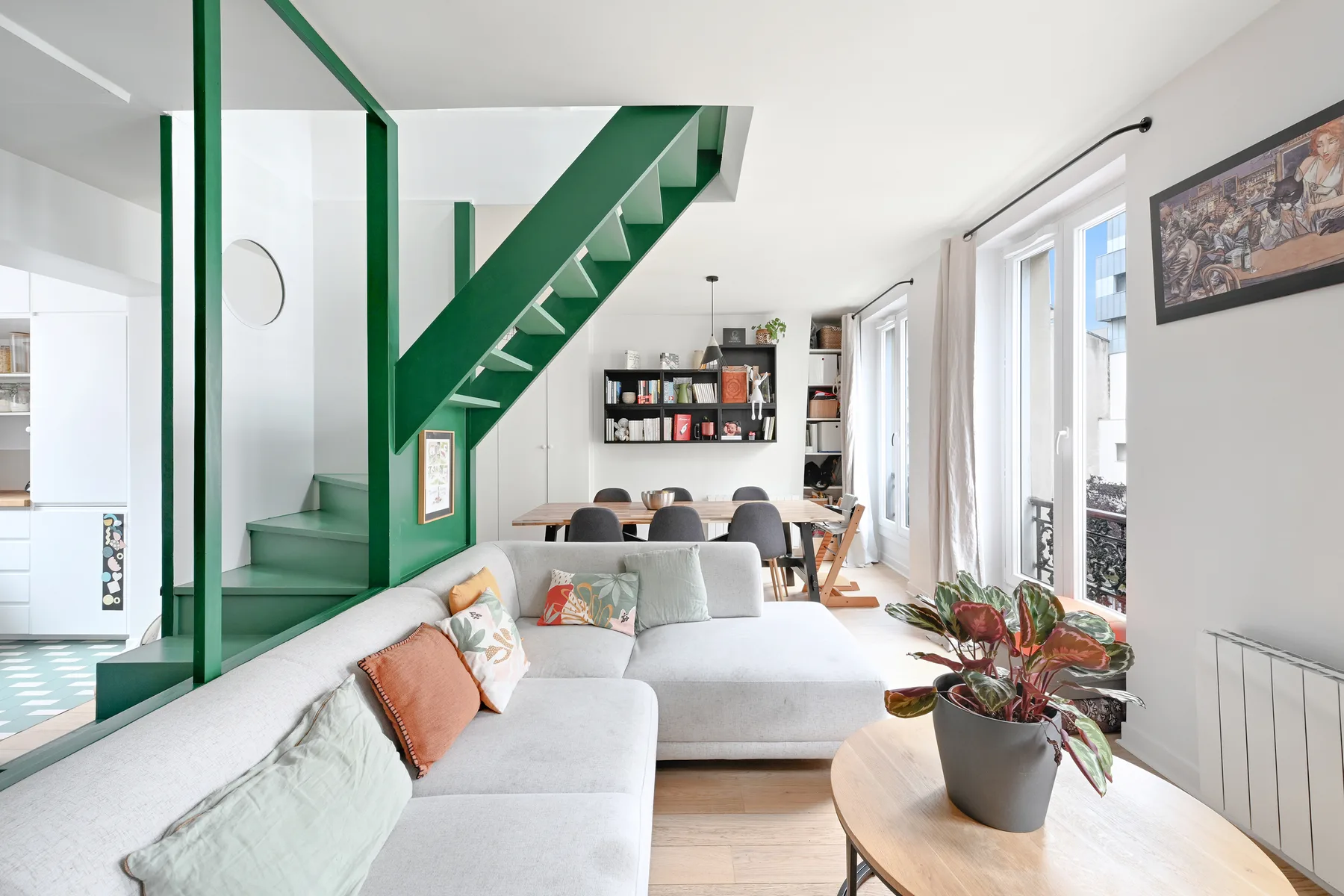A bright living room with sectional seating beneath a green staircase.