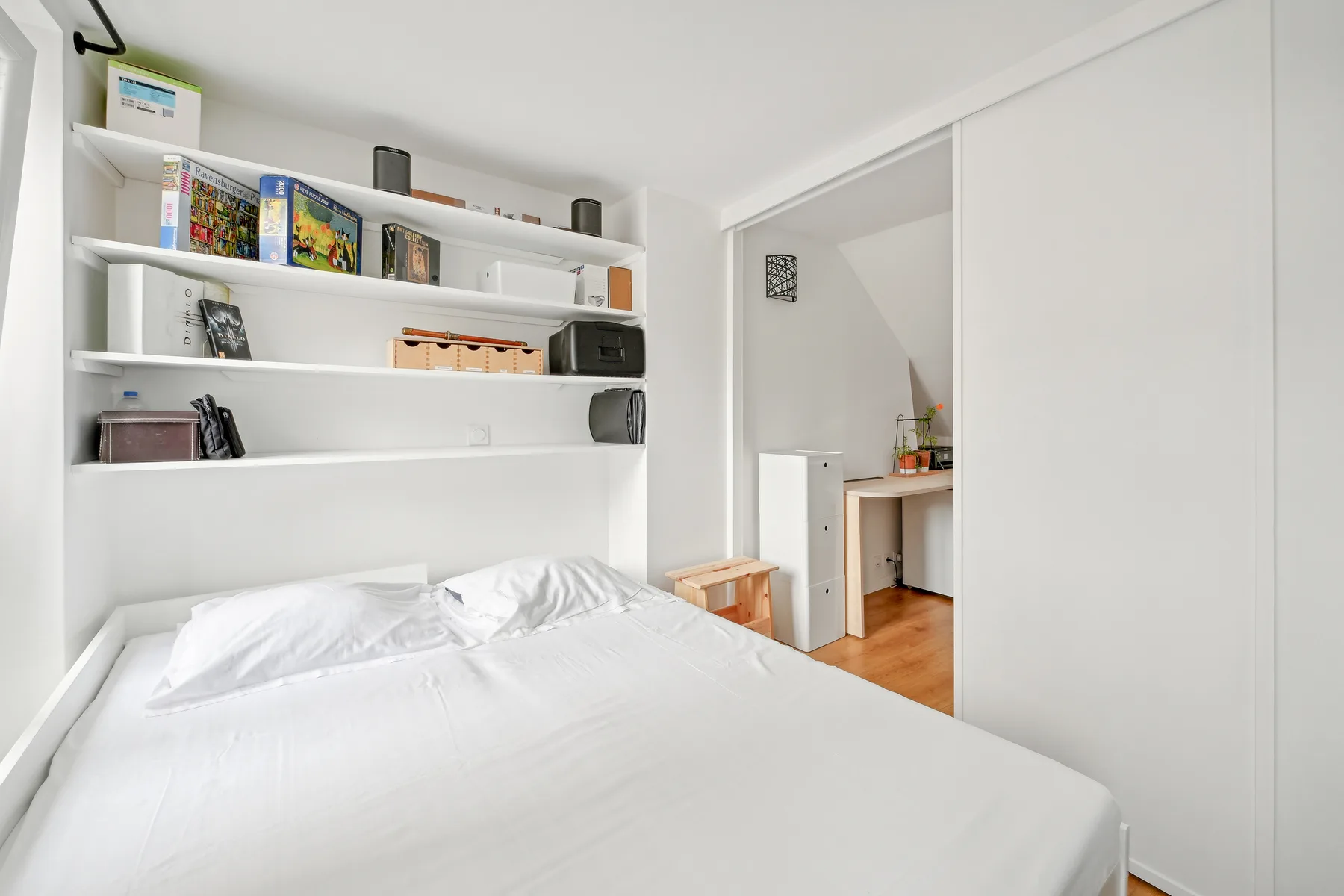 A bedroom with a white bed and open shelves along the wall.