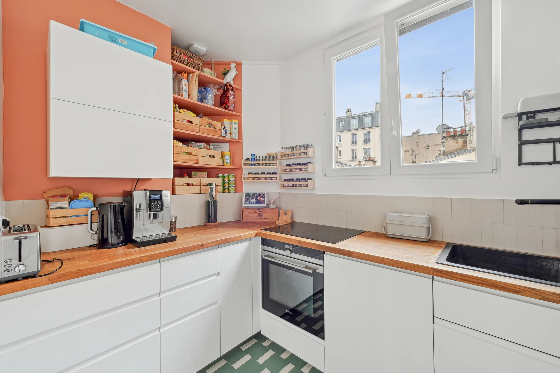 A bright kitchen with white cabinets, wooden countertops, and large windows.