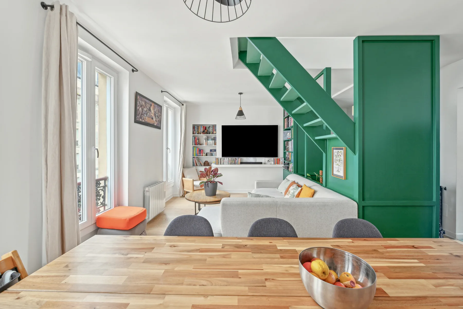 A bright living room with a dining table, seating, and a green staircase.