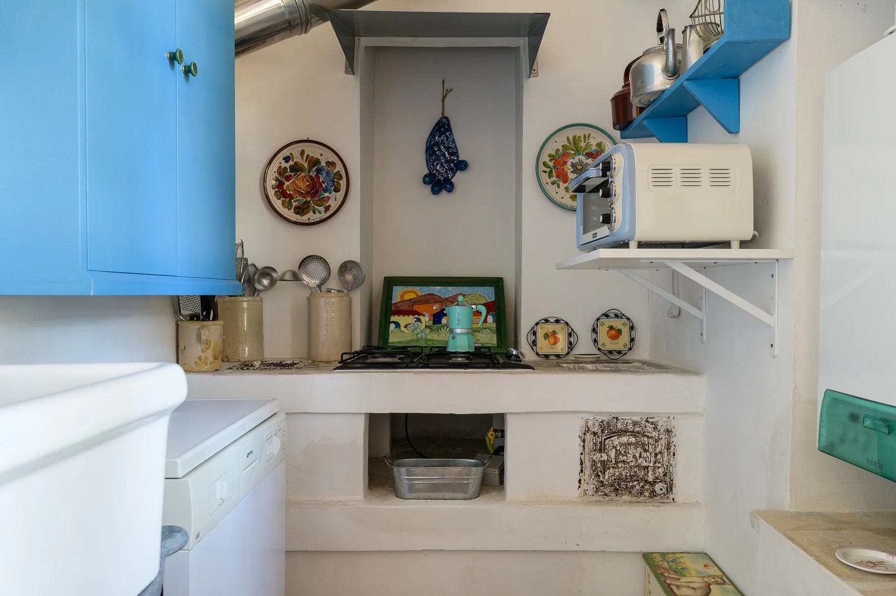 A compact kitchen with blue cabinets, a stovetop, and countertop appliances.
