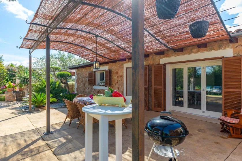 A shaded outdoor patio with a dining table, seating, and sliding glass doors.