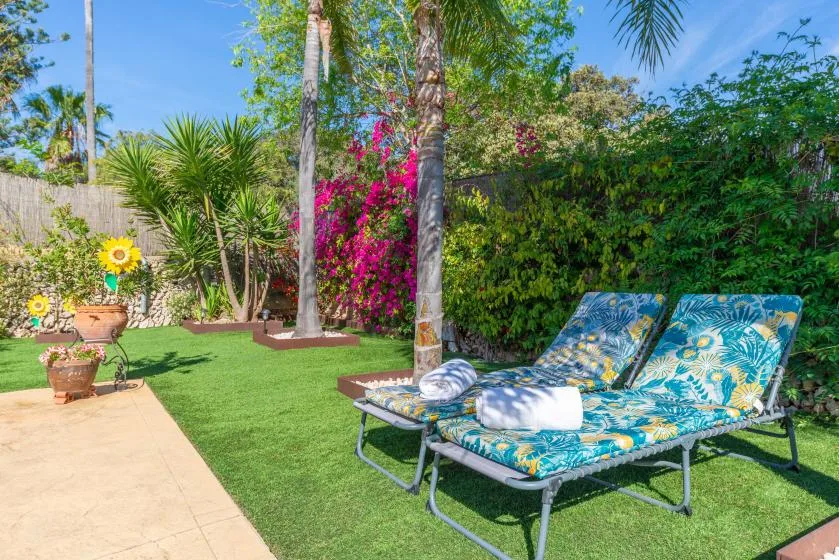 A sunny garden seating area with colorful lounge chairs beside flowering plants.